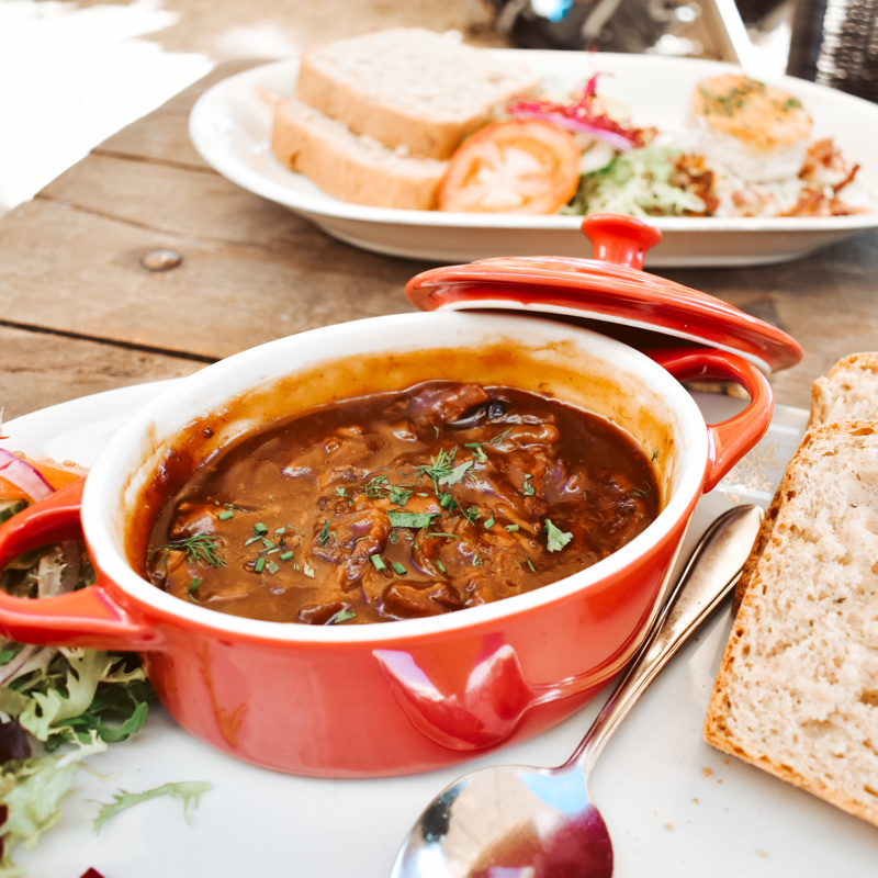 Een bord met een potje zuurvlees, geserveerd met brood en garnering