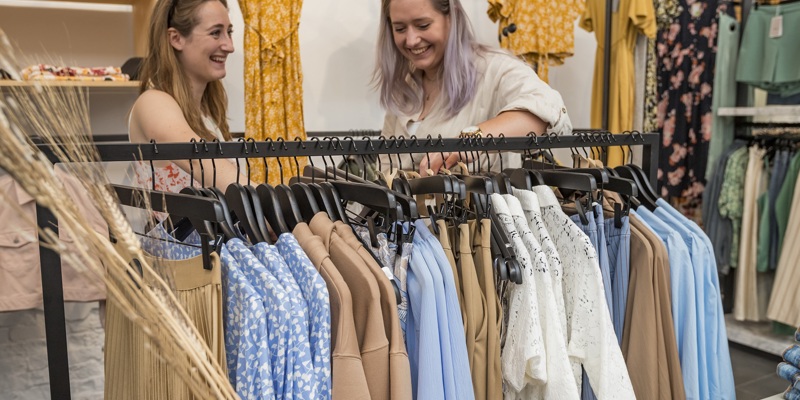 Twee vrienden kijken lachend tussen de kleding in een kledingrek